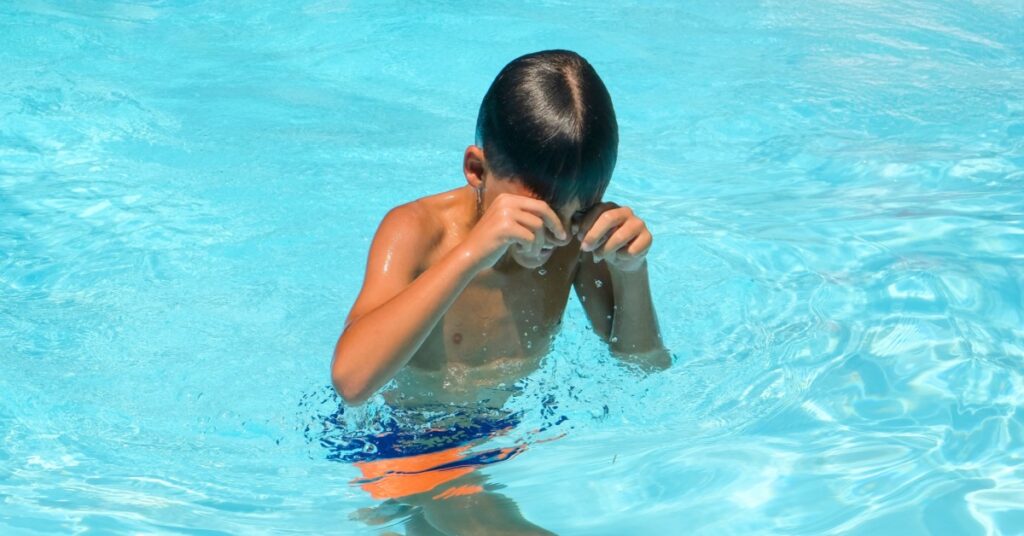 boy rubbing eyes in pool